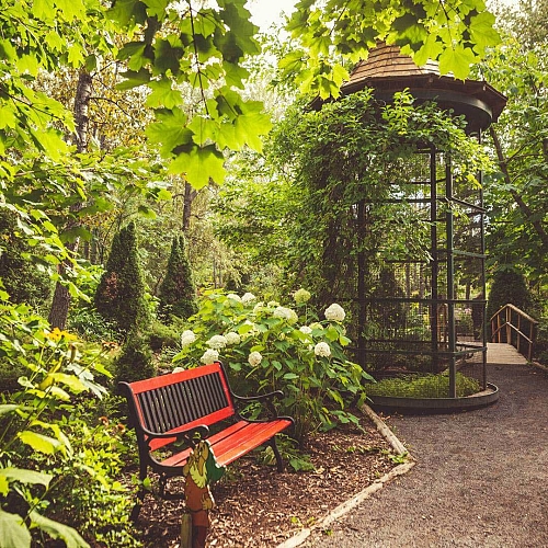 Aire de repos avec banc en bois entouré de plantes et volière à papillons aux Jardins de Doris