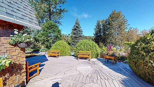 Galerie en bois placé de sorte à faire une mosaïque en fleur et quelques bancs en bois à proximité de l’entrée d’un petit bâtiment en bardeau de cèdre.
